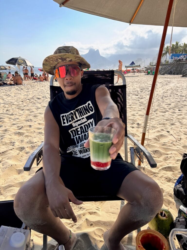 Skylar DeRouen seated under a beach umbrella at Arpoador